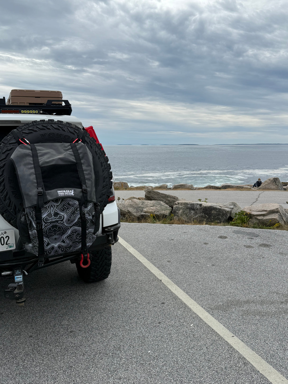 Small vehicle on a road next to a body of water with clouds in the sky
