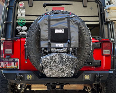 Red Jeep Wrangler with a spare tire cover and additional gear on a rocky terrain